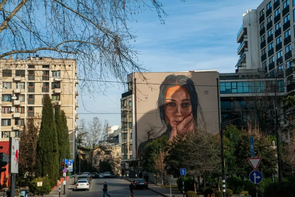 Rue de Tbilissi avec fresque murale géante, image qui illustre les balades urbaines et découvertes artistiques à faire en hiver.