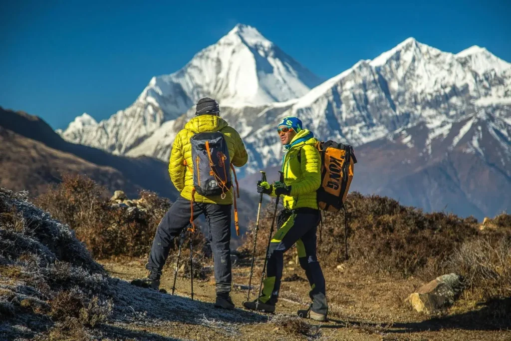 Deux randonneurs en veste jaune fluo avec sacs et bâtons, image qui illustre le trekking en Géorgie pour débutants dans un décor de sommets enneigés.