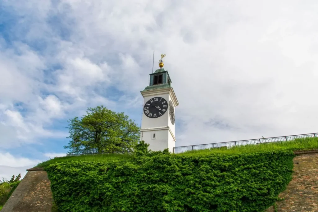 Tour blanche avec horloge romaine sur colline verdoyante, reflet des incontournables architecturaux à découvrir en Voïvodine.