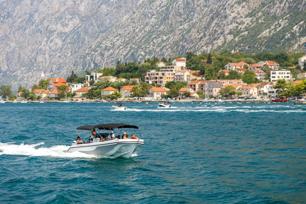 Bateau blanc glissant sur mer turquoise devant village, image qui traduit l’ambiance d’un voyage au Monténégro.
