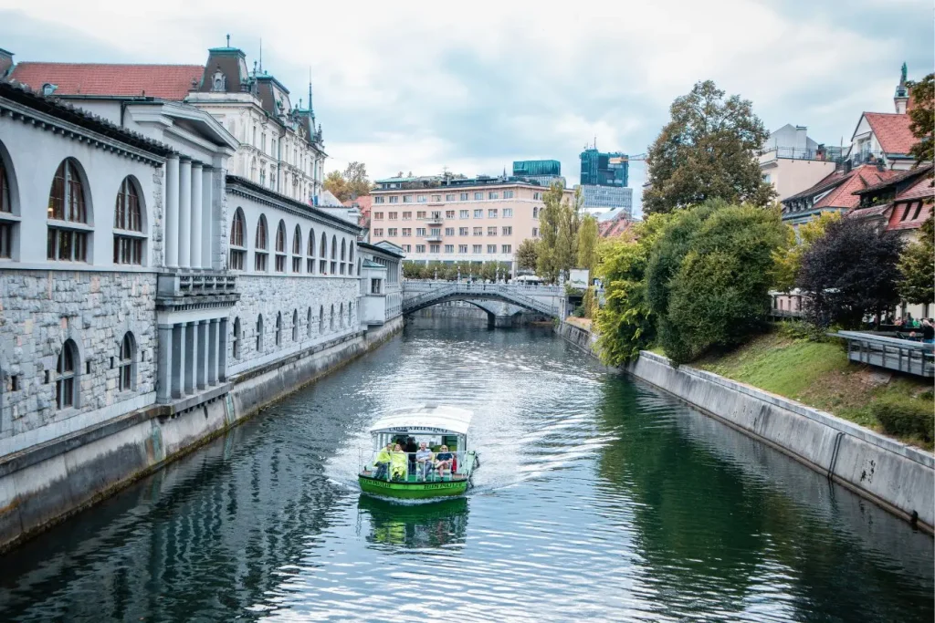 Bateau vert et blanc avançant sur canal bordé de façades historiques, image qui illustre une étape incontournable lors d’un séjour de cinq jours en Slovénie.