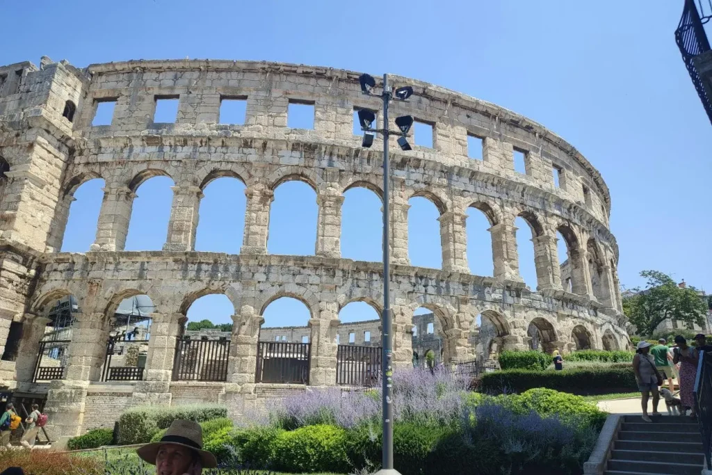 Vue extérieure de l’amphithéâtre romain de Pula avec arches en pierre et jardins fleuris, reflet d’un site incontournable à visiter en Croatie.