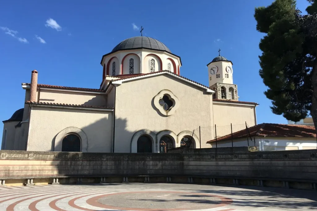 Église à dôme central beige et rouge sur ciel bleu, reflet du patrimoine architectural à découvrir en visitant Kavala en Grèce.