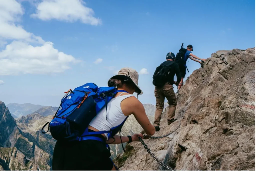 Trois randonneurs gravissent une pente rocheuse avec une chaîne, image d’une randonnée au Mont Olympe dans un décor montagneux impressionnant.