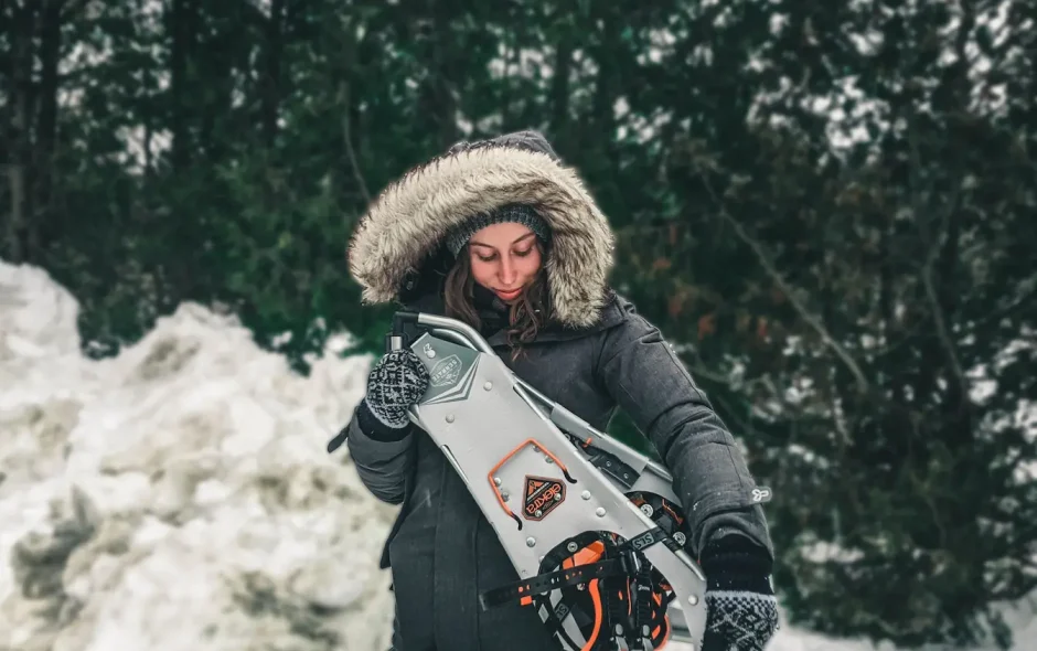 Personne en manteau sombre tenant raquettes Atlas, image qui illustre les raquettes à neige pour débutant.