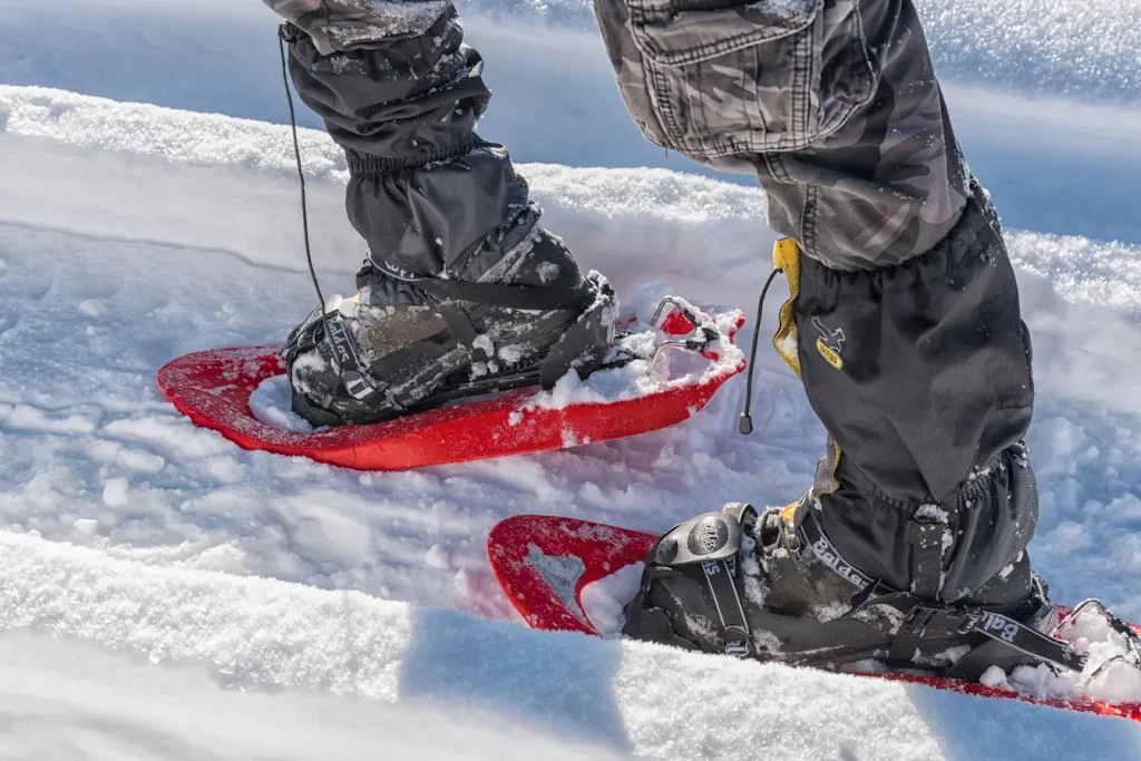 Gros plan sur jambes équipées de raquettes rouges, image qui illustre les raquettes à neige pour débutant.