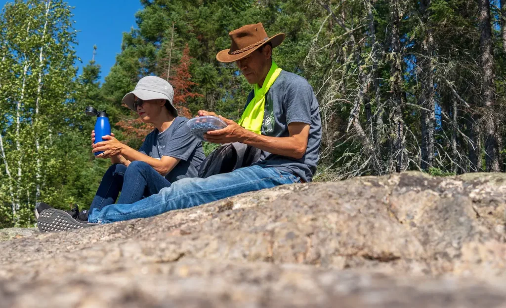 Deux personnes assises sur rocher en forêt partageant eau et fruits, reflet d’un repas simple et convivial en randonnée.