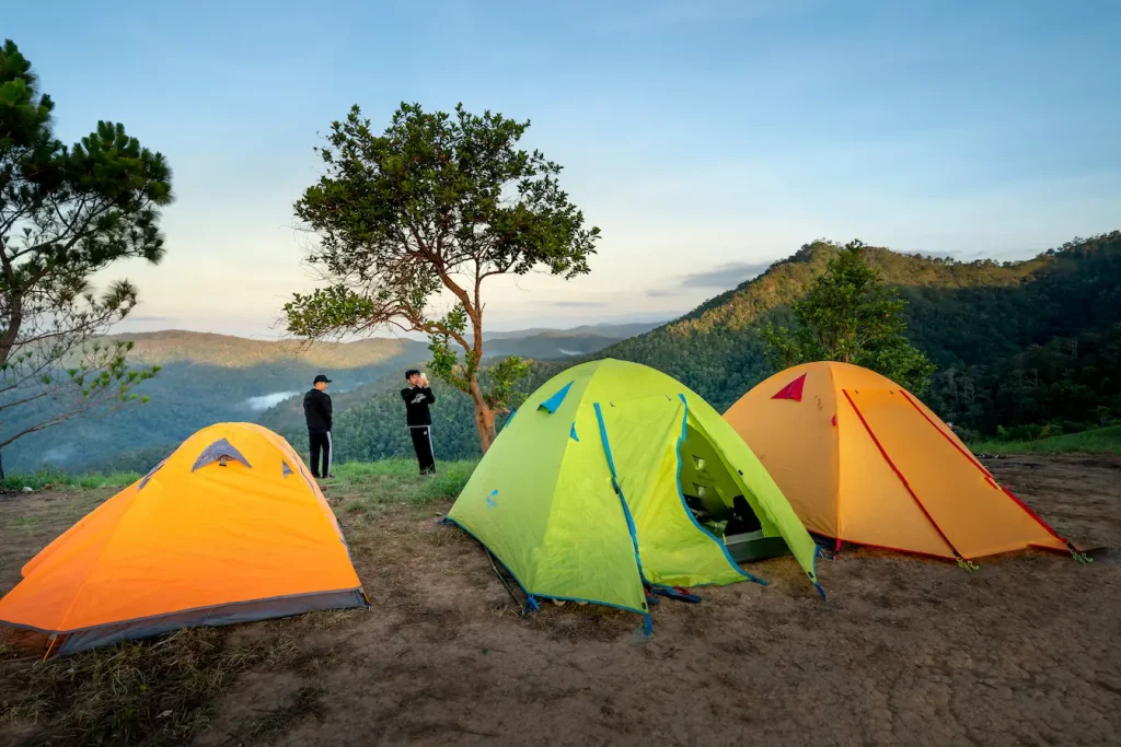 Trois tentes colorées installées sur crête herbeuse, reflet des pratiques d’entretien nécessaires pour prolonger la durée de vie d’une tente de camping.