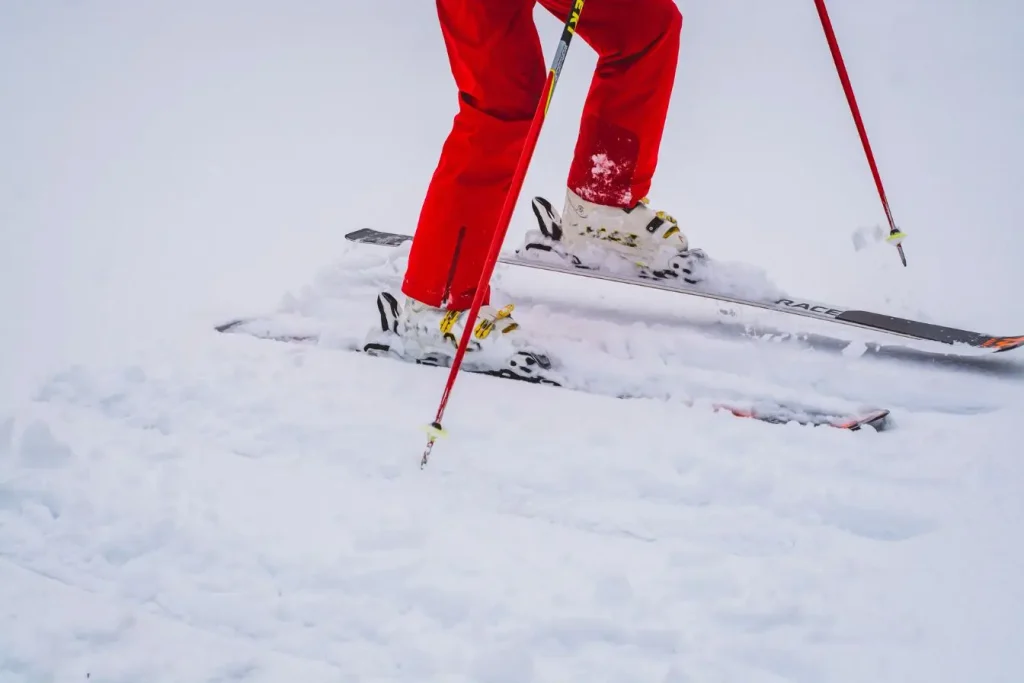 Skieur avançant sur une pente enneigée avec des chaussures techniques fixées aux skis, illustrant l’importance de choisir des crampons adaptés aux terrains glacés