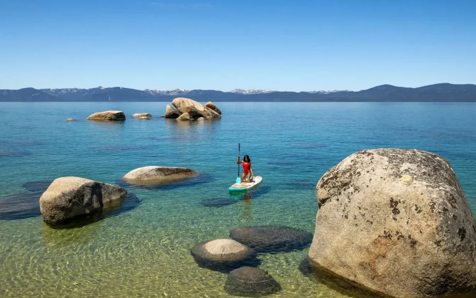 Personne debout sur un paddle dans une eau calme et cristalline près de gros rochers, une situation idéale pour débuter le paddle en mer en douceur