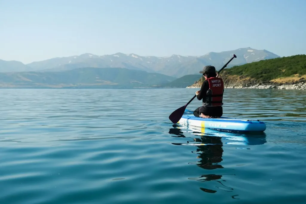 Personne debout sur un paddle dans une eau calme et cristalline près de gros rochers, une situation idéale pour débuter le paddle en mer en douceur