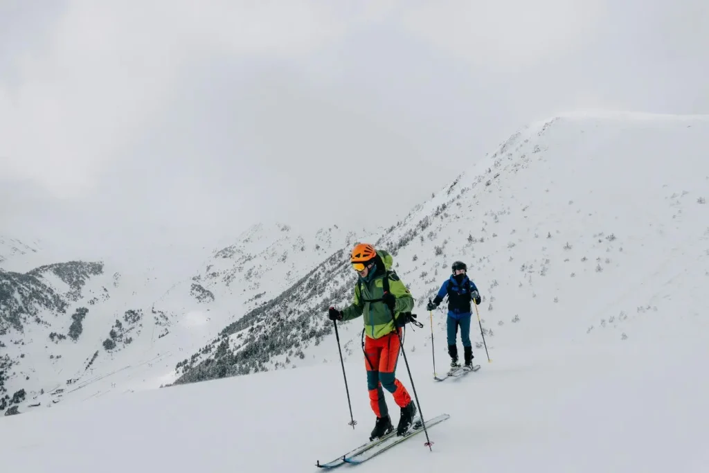 Deux skieurs progressent sur une pente enneigée en montagne, suivant un itinéraire accessible pour s’initier au ski de randonnée en terrain hivernal