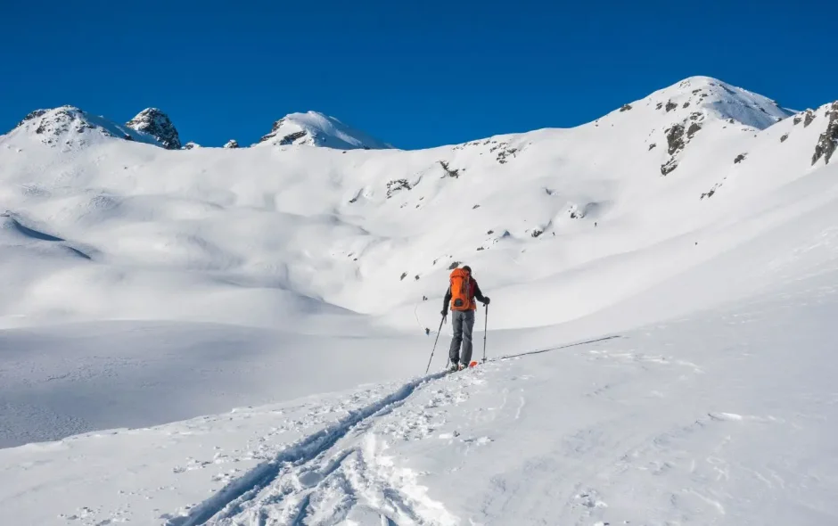 Personne avançant à skis sur un relief enneigé sous un ciel dégagé, une scène idéale pour s’initier au ski de randonnée en montagne